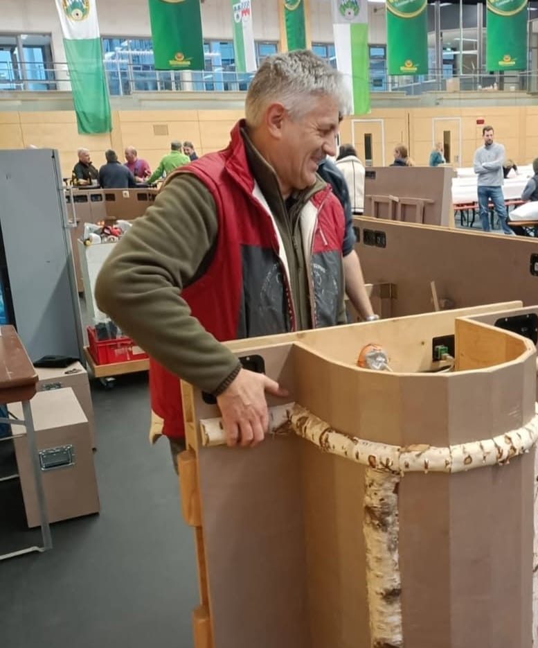 Sepp stellt beim Aufbau ein rundes Barelement mit Birkenstamm auf
