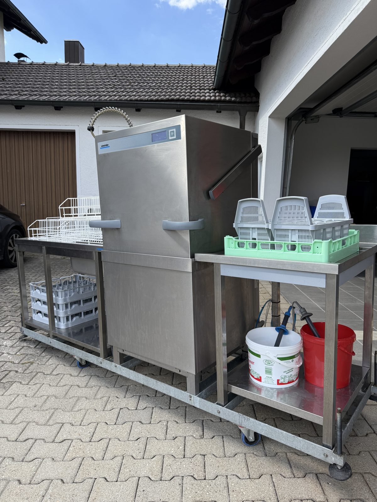 Haubenspülmaschine auf fahrbarem Gestell mit Körben und Spülmittel
