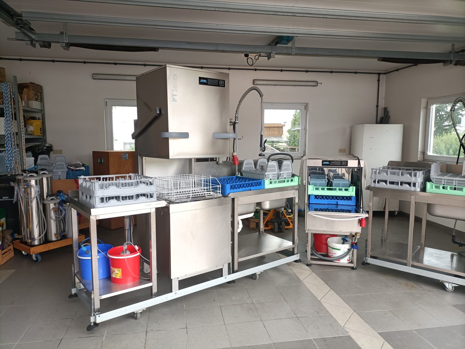 Geöffnete Haubenspülmaschine mit Körben für Gläser, Teller und Besteck davor