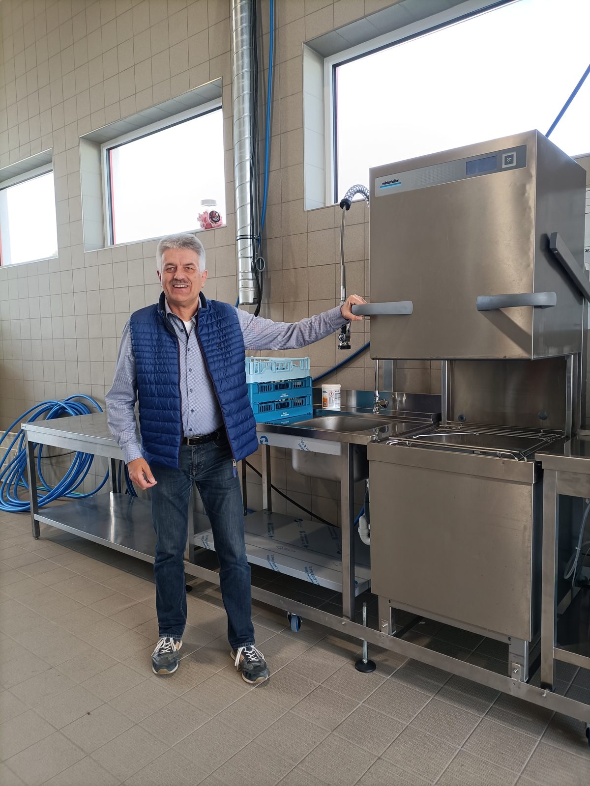 Sepp neben der Haubenspülmaschine mit langem Edelstahl-Spültisch in einer Halle